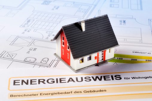 Ein Energieausweis, Baupläne und ein Miniaturhaus in der Nahaufnahme.